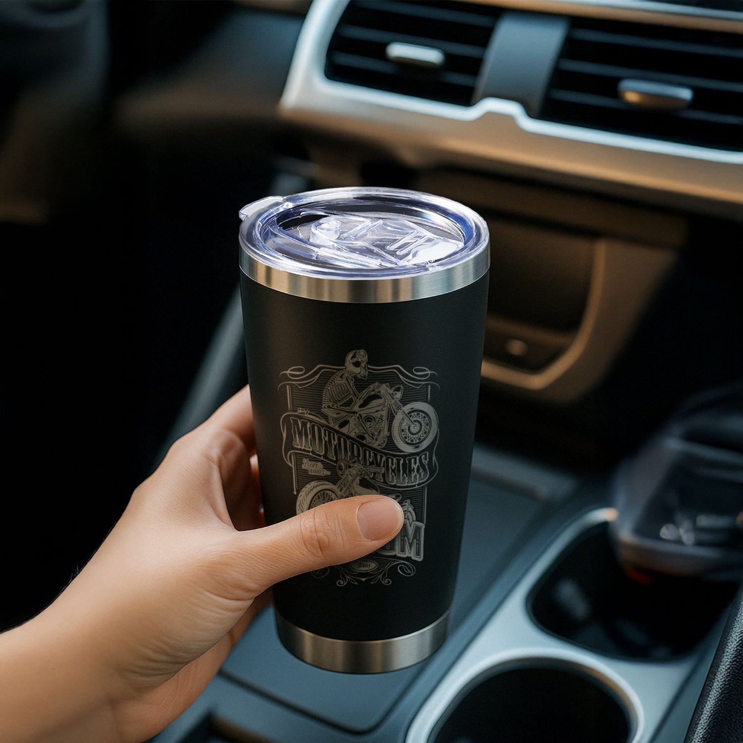 A man sits in the car and holds a black tumbler with motorbike engraving.