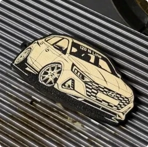 Un maker usa un grabador láser para grabar un gráfico detallado de un automóvil en un llavero flexible de TPU impreso en 3D.