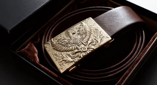 A leather belt with an intricately engraved eagle buckle in gift packaging.