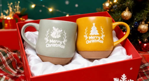 Two Christmas-themed ceramic mugs with engraved festive designs presented in a red gift box.