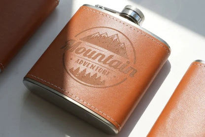 LaserPecker LP2 Plus professional laser engraving on a brown leather hip flask sleeve, featuring a detailed "Mountain Adventure" outdoor-themed logo with deep, clean contrast.