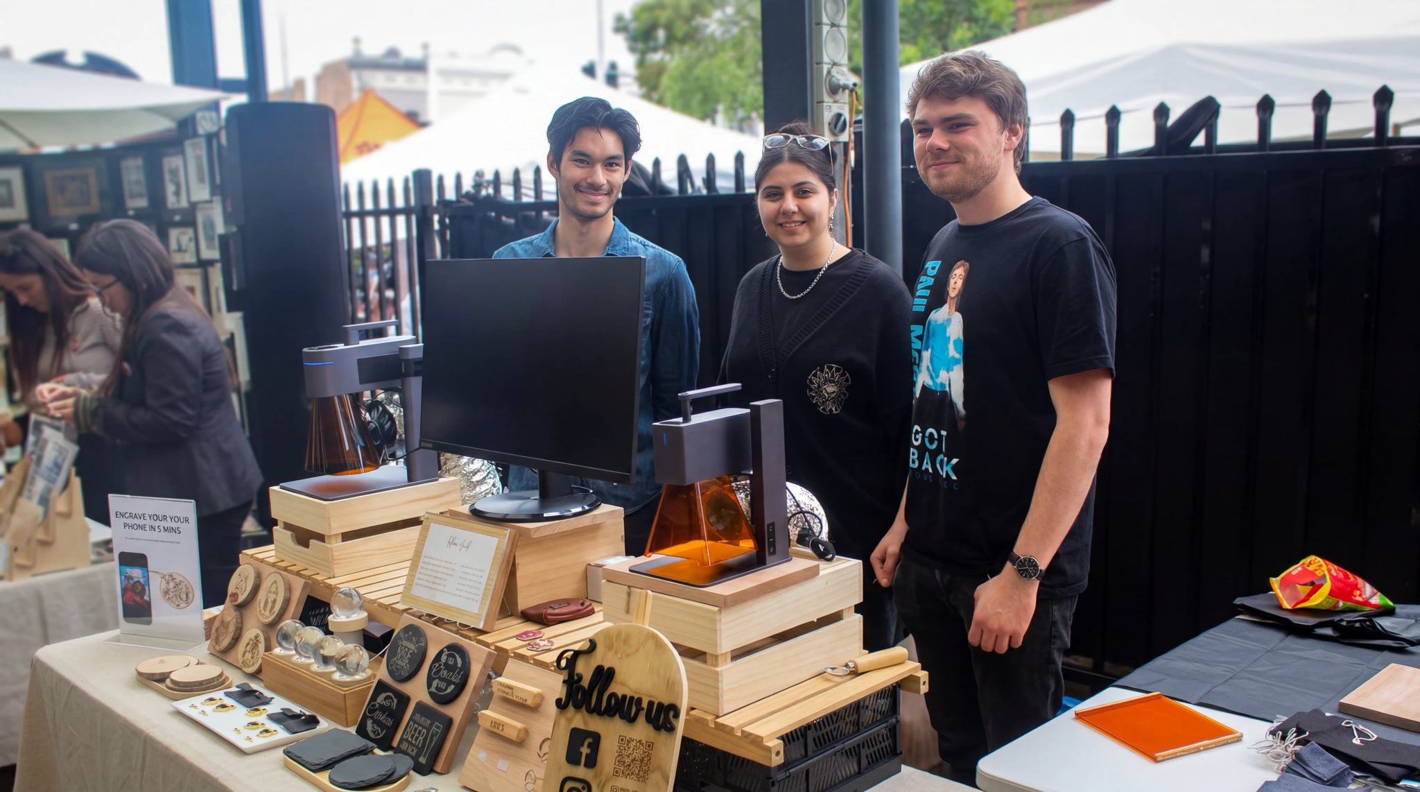 Trois vendeurs présentent des machines et des créations artisanales sur leur stand.