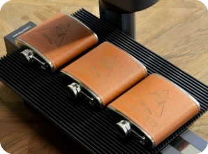 LaserPecker LP2 Plus performing synchronized batch engraving on premium leather-wrapped hip flasks using the Slide Extension.