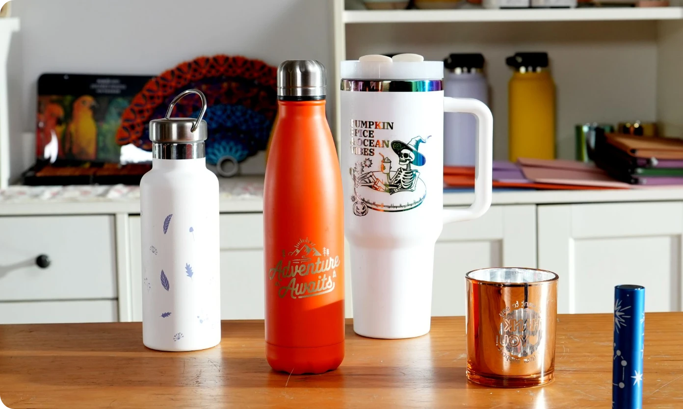 Custom laser engraved metal water bottles and tumblers featuring intricate skeleton and nature designs, showcasing the versatility of the LP2 Plus laser engraver on cylindrical surfaces.
