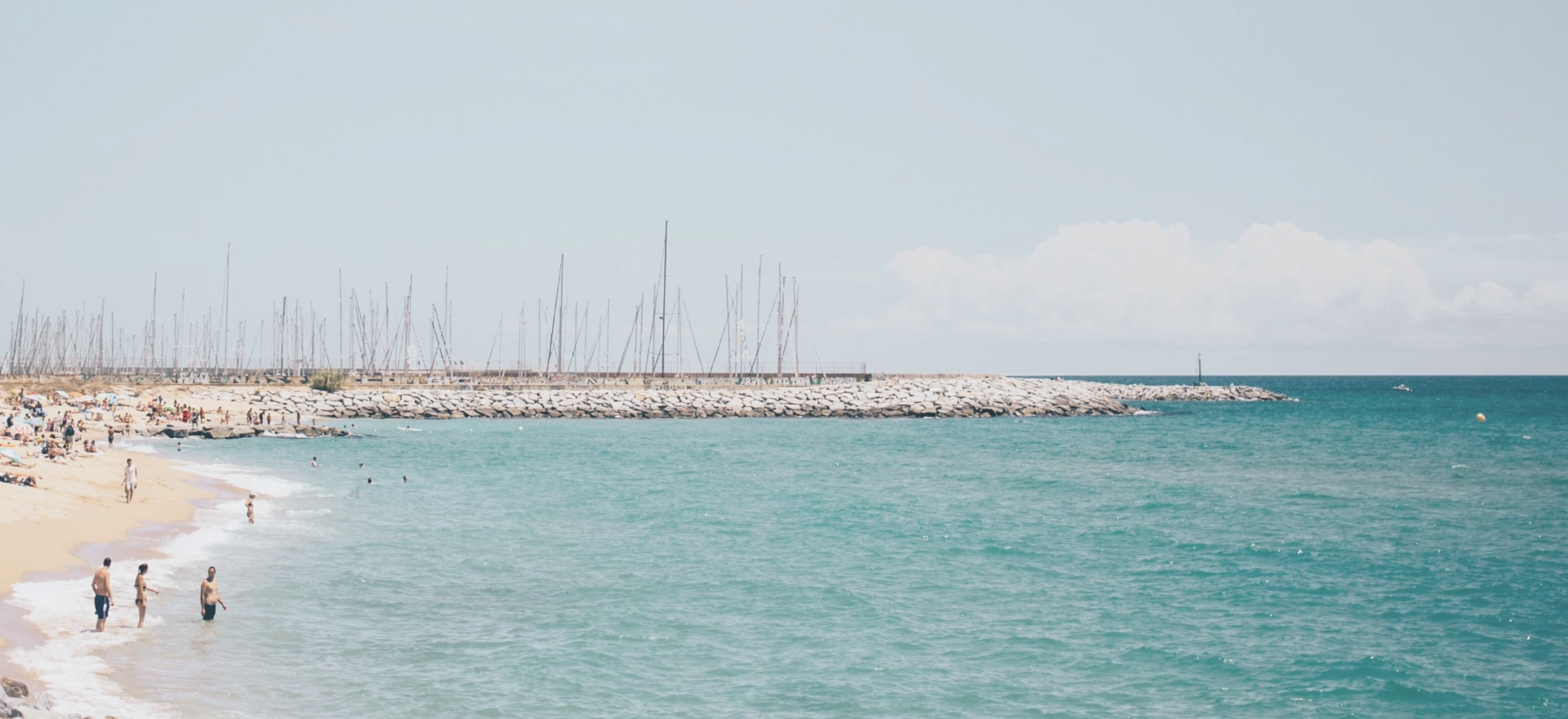 Une mer d’un bleu éclatant et une plage de sable doré où de nombreuses personnes profitent d’activités de loisirs.