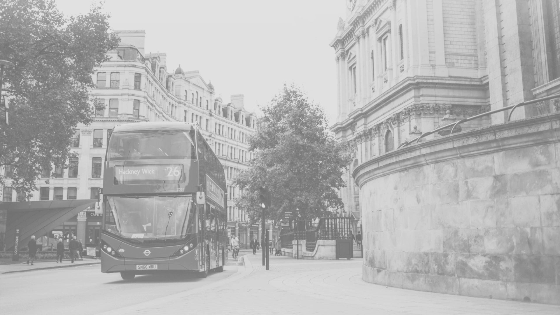 Une rue au Royaume-Uni avec un bus rouge circulant sur la route, entourée de bâtiments historiques blancs et de quelques passants dispersés.