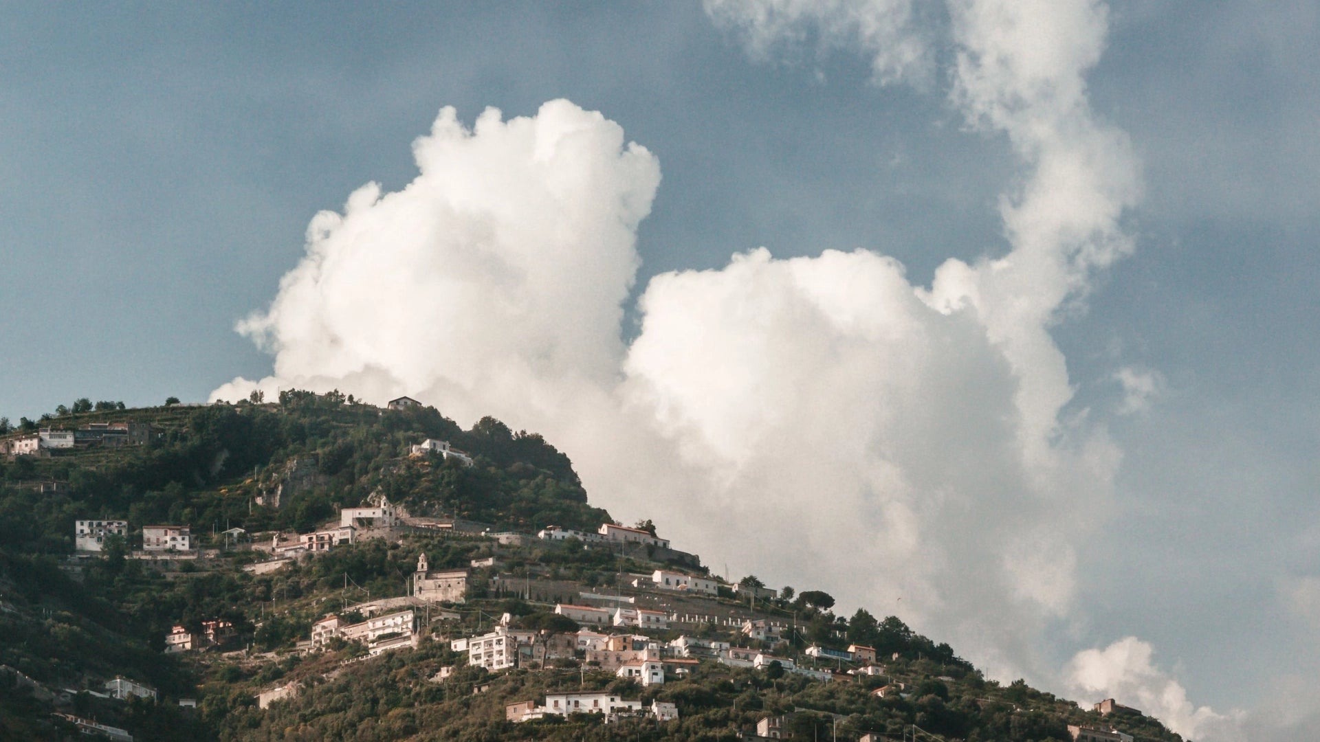 Des collines côtières en Italie avec plusieurs maisons surplombant un vaste ciel rempli de nuages.