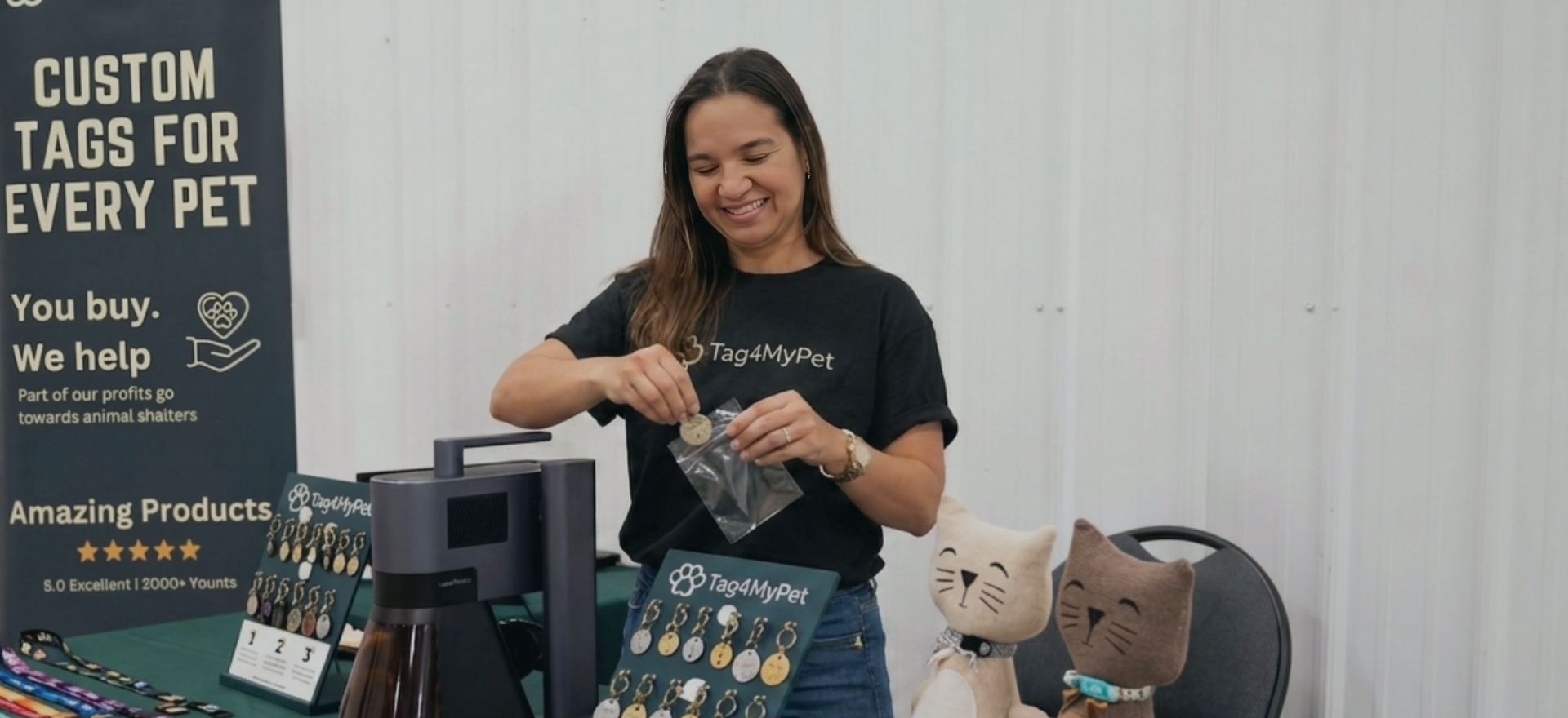 Une femme présentant des médailles pour animaux personnalisées réalisées avec une machine LaserPecker sur un stand de marché artisanal.